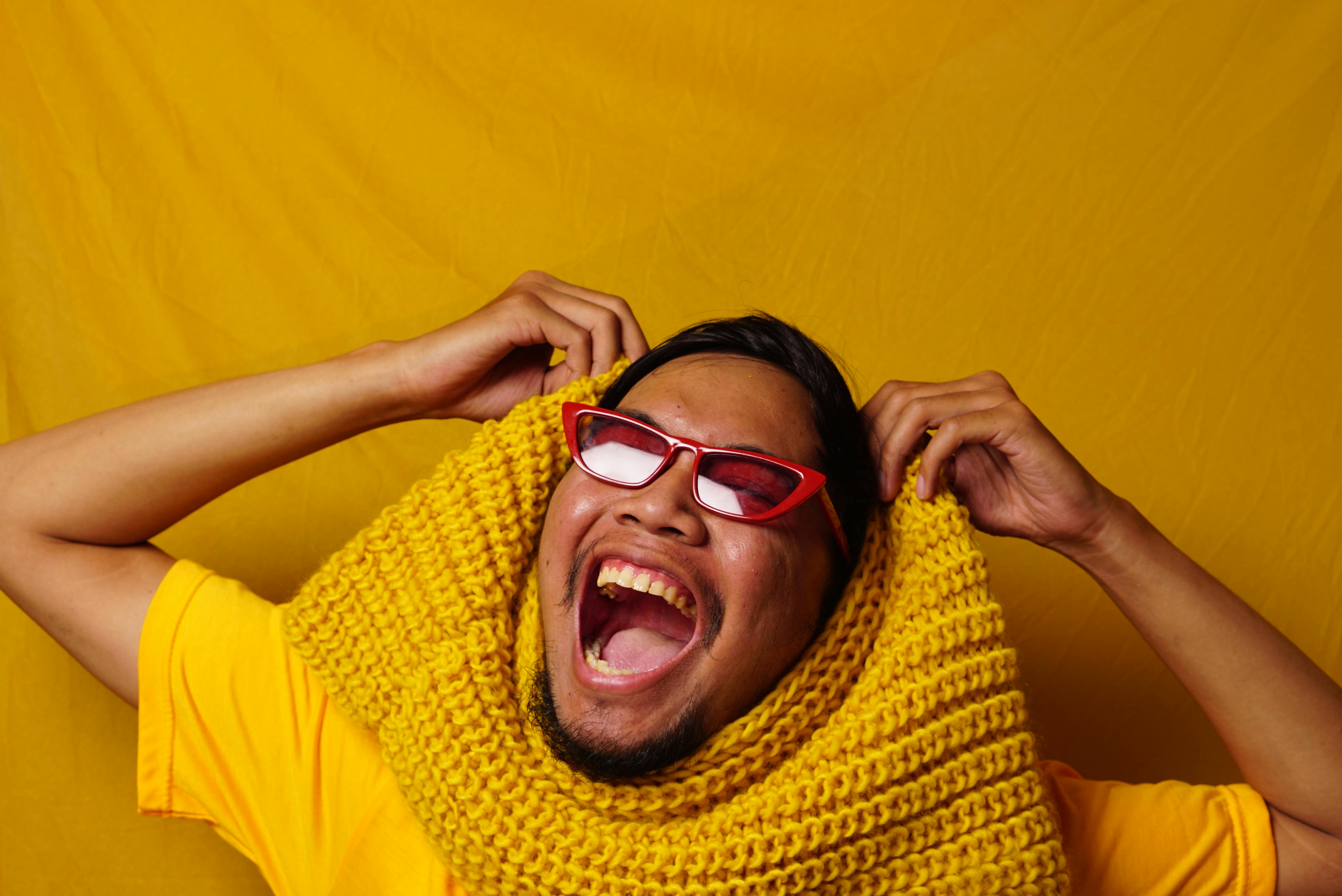 Miễn phí Người đàn ông đeo kính đỏ và quàng khăn vàng đang cười tươi, nổi bật trên nền sáng, toát lên vẻ hạnh phúc. Ảnh lưu trữ