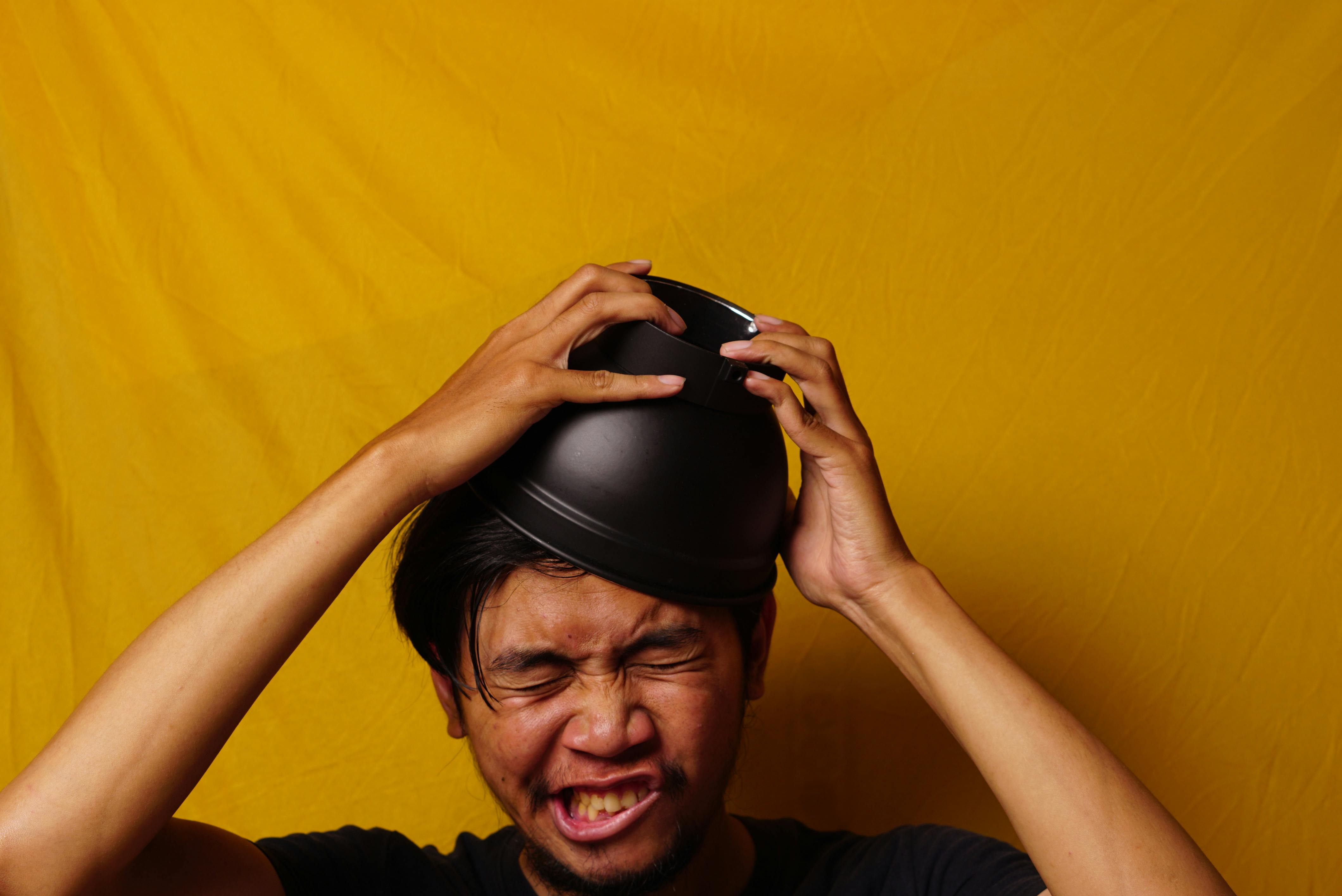 grátis Retrato humorístico de um indonésio usando uma tigela como chapéu contra um vibrante fundo amarelo. Foto profissional