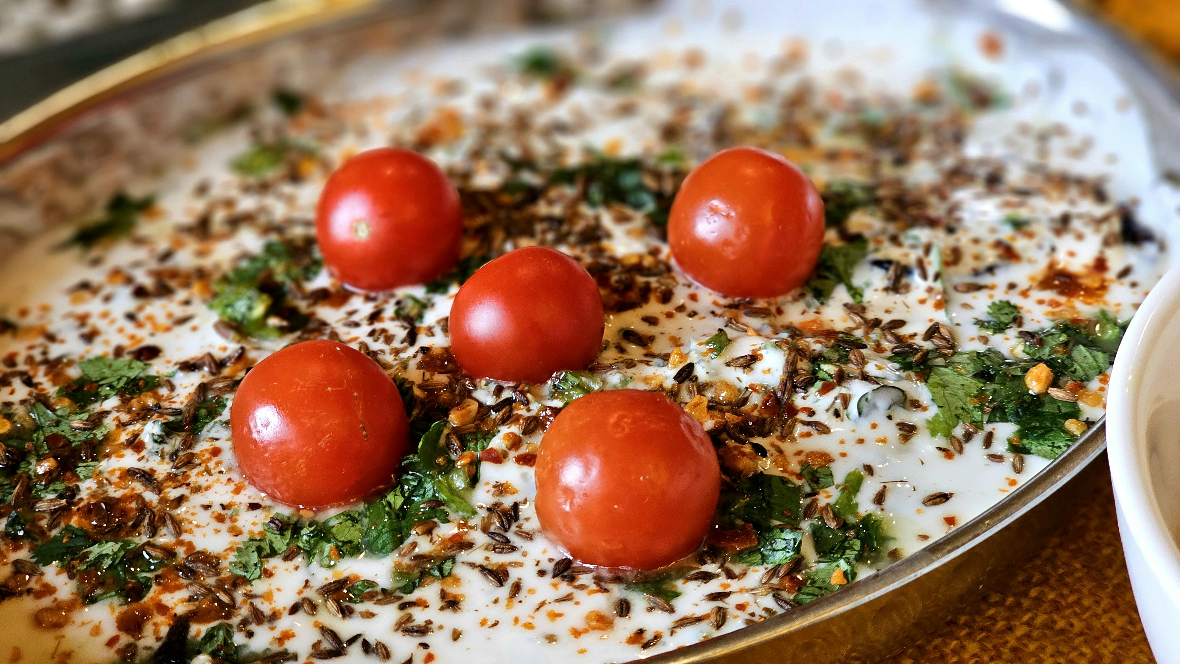 A vibrant yogurt dish topped with cherry tomatoes, herbs, and spices, perfect for culinary inspiration. - Photo by Muhammad  Khawar Nazir on Pexels