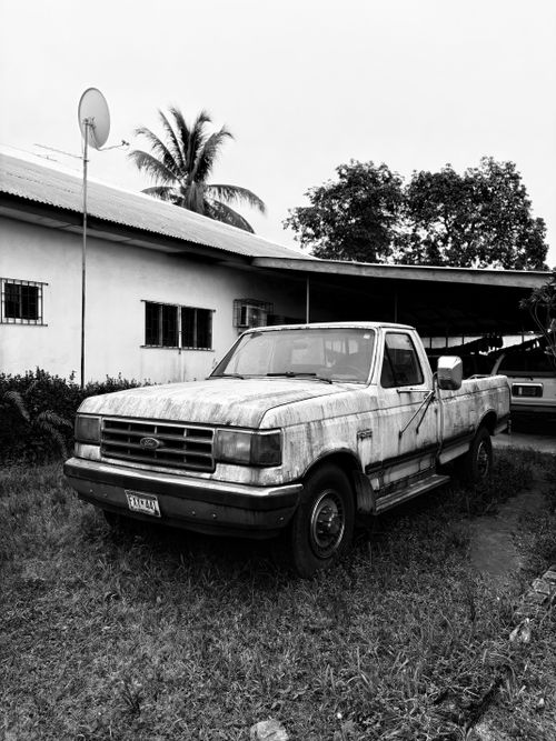 Free A black and white image of an old rusty truck near a tropical residence. Stock Photo