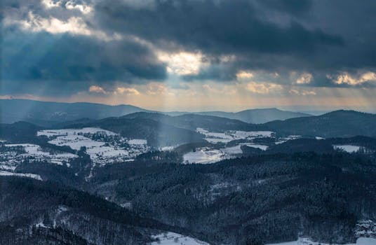 Captivating view of Odenwald's snow-covered hills under dramatic clouds with sun rays breaking through.
