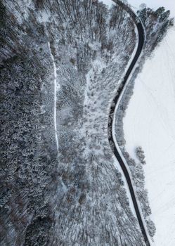Aerial view of snow-covered forest and winding road during winter in Germany.