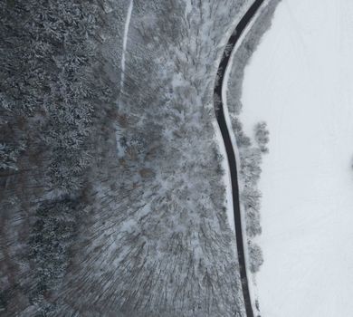 Aerial view of a snow-covered forest and curving road during winter.