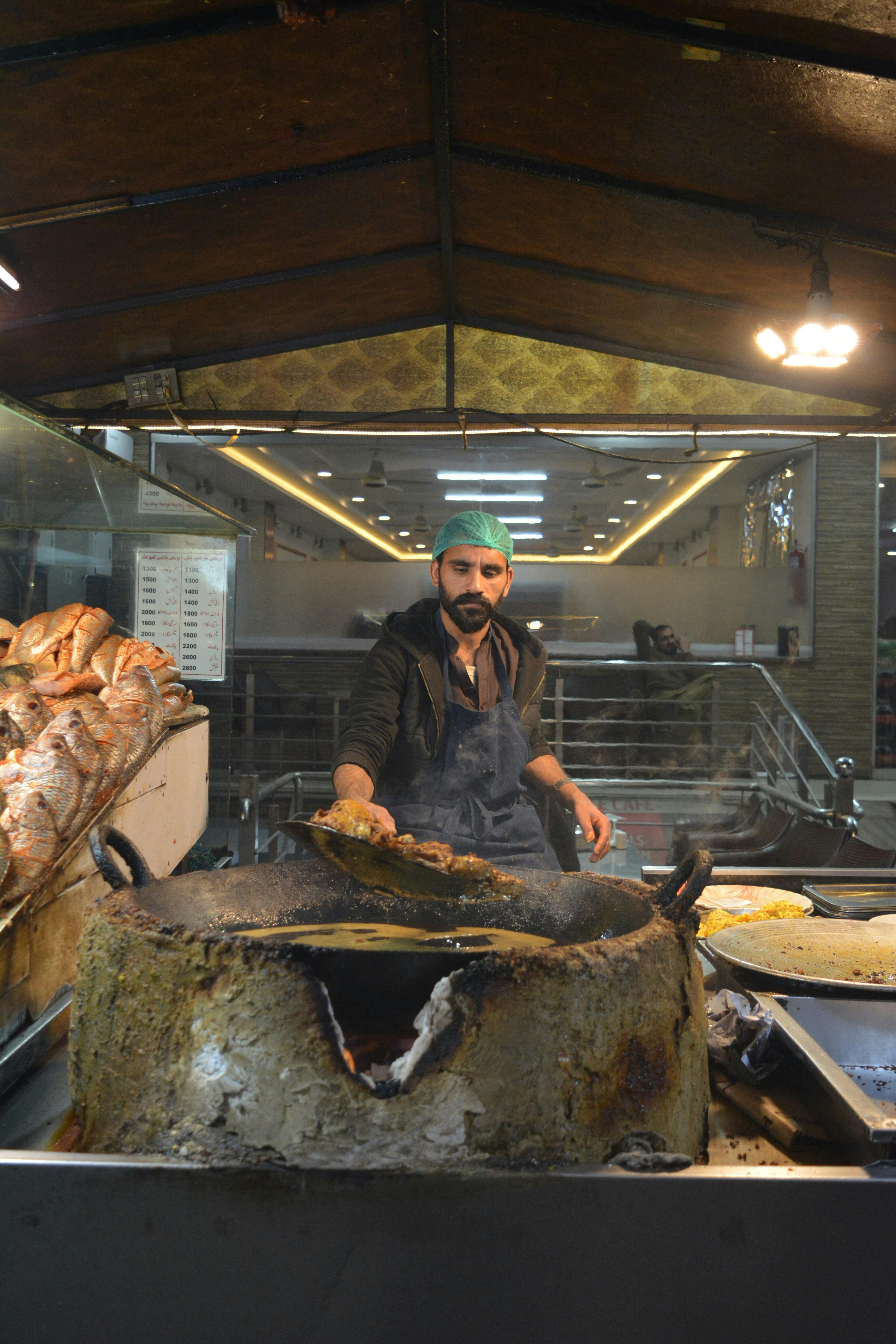 Street food vendor grilling fish in Hassanabad market, Punjab, showcasing local culinary culture.