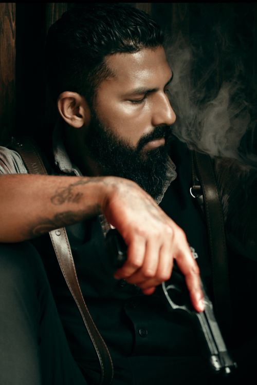 Free Dramatic portrait of a bearded man with a tattoo holding a revolver, enveloped in smoke. Stock Photo