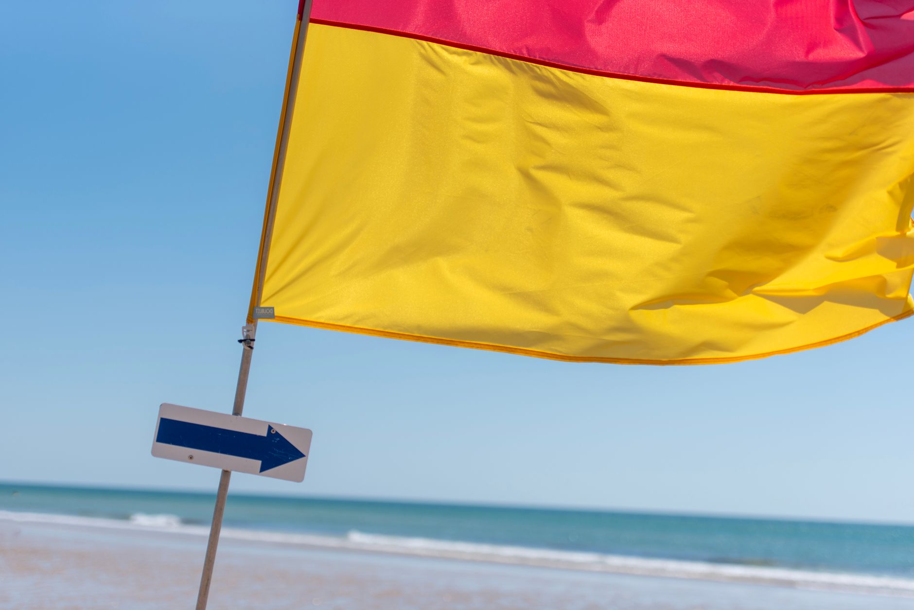 Vibrant red and yellow flag with arrow sign on a sunny beach.
