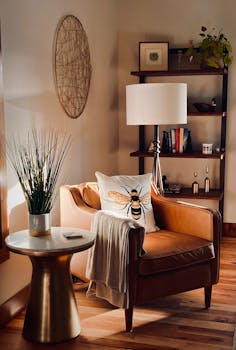 Sunlit corner of a living room with a leather chair, embroidered bee pillow, and decor accents.