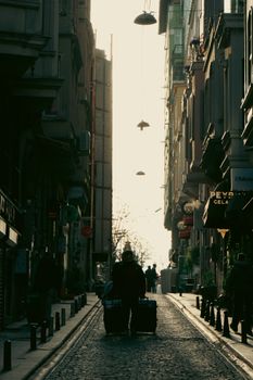 Silhouette of pedestrians walking through a narrow urban street during sunset, creating a dramatic contrast.