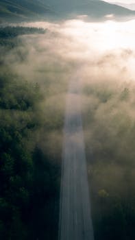 Aerial view of a foggy road through forests and mountains in Orhaneli, Bursa, Türkiye at dawn.