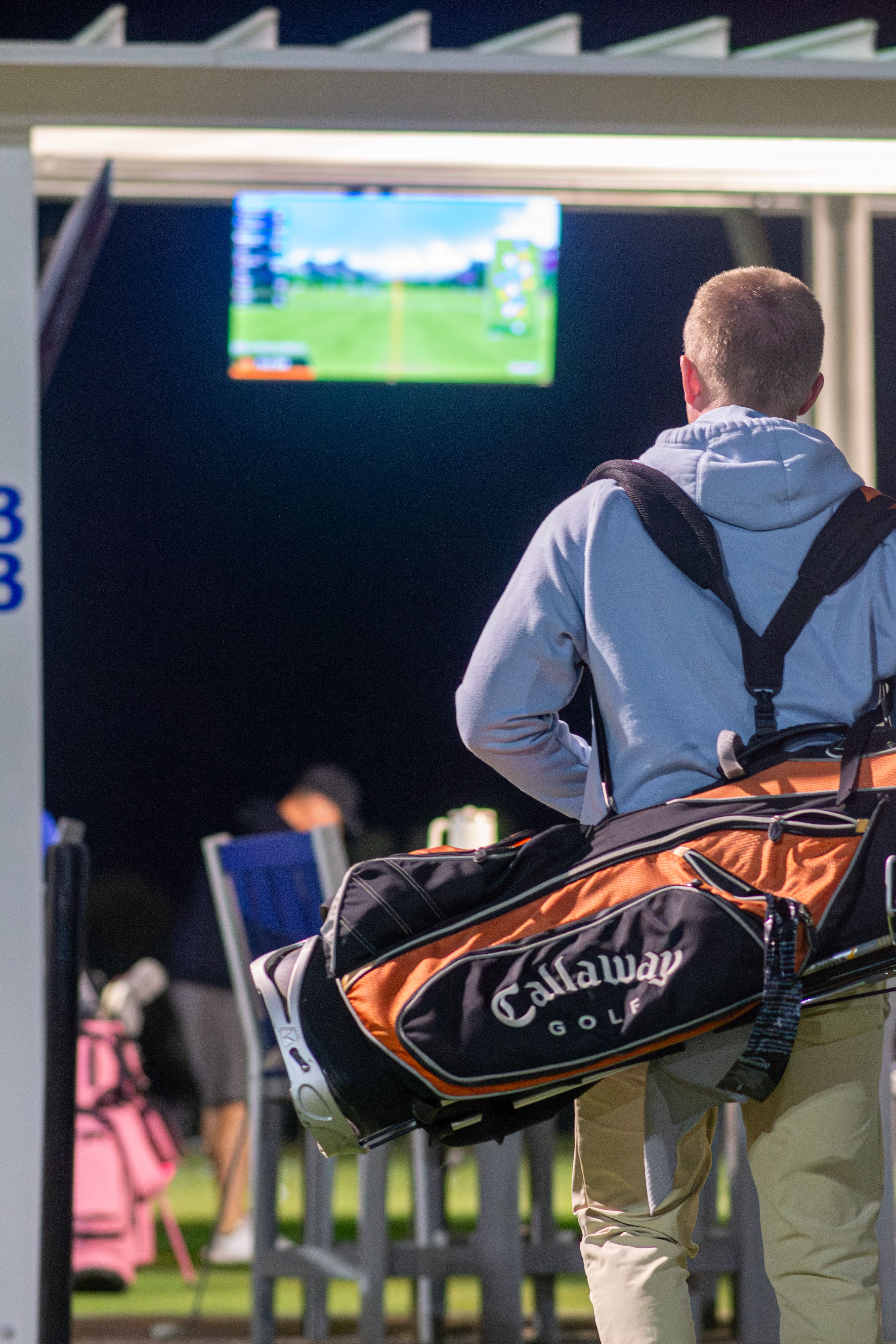Golfer carrying Callaway bag at night driving range, focused on practice.