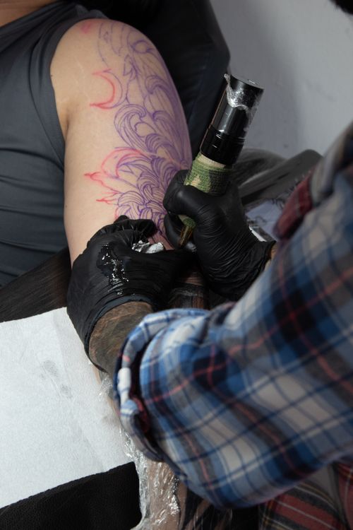 Free A tattoo artist is creating an intricate design on a client's upper arm using tattoo equipment. Stock Photo