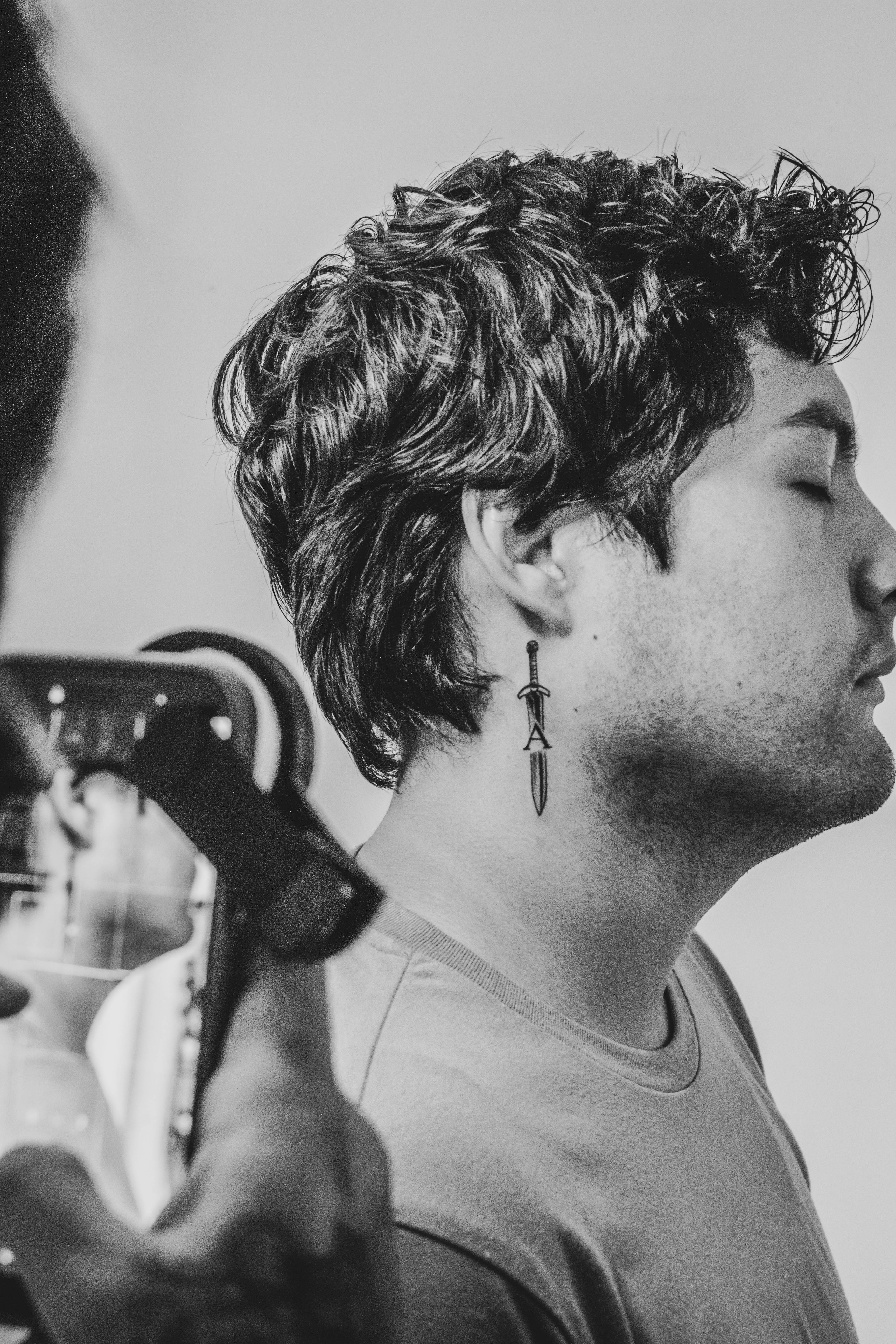 Black and white profile portrait of a man wearing unique dagger earrings during a photoshoot.