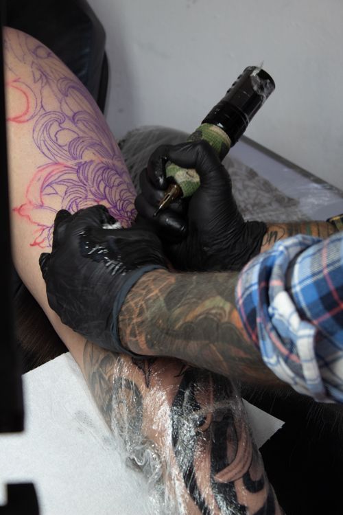 Free Tattoo artist working on detailed floral design on a person's leg. Stock Photo