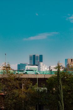 Skyline view featuring modern skyscrapers behind a busy highway with lush greenery in the foreground.