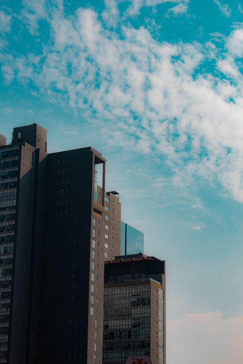 Free Tall modern skyscrapers reach towards a vibrant blue sky with scattered clouds. Stock Photo