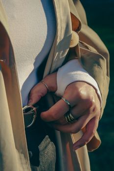 Close-up of a person wearing rings and a beige coat in an outdoor setting, capturing autumn vibes.