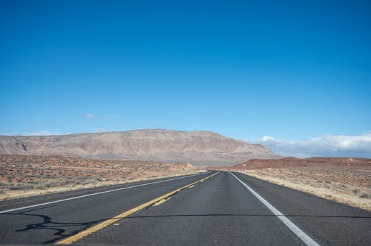 Expansive desert highway leading to rugged mountains under a clear blue sky.