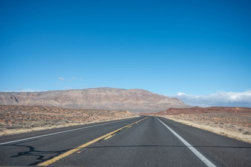 Free Expansive desert highway leading to rugged mountains under a clear blue sky. Stock Photo