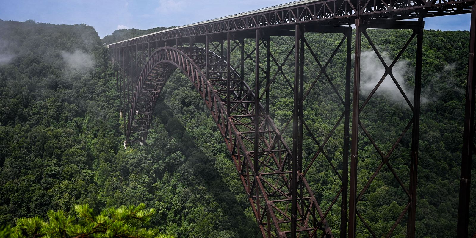 The New River Gorge Bridge surrounded by lush summer greenery and mist