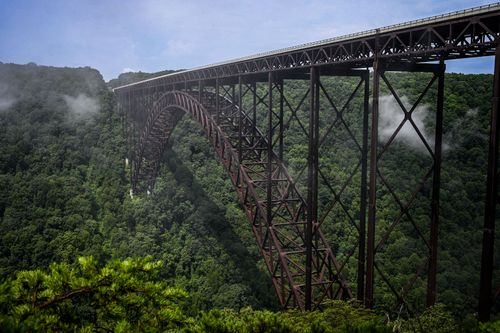 Free A breathtaking view of the New River Gorge Bridge surrounded by lush summer greenery and mist. Stock Photo