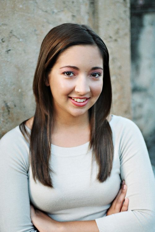 Free A young woman with long hair smiling while leaning against a textured stone wall. Stock Photo