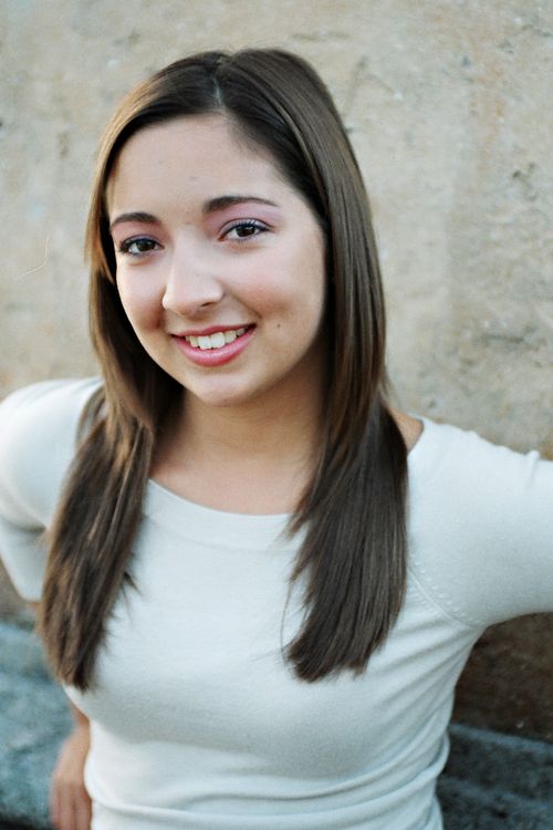 Free A young woman smiles warmly at the camera with a textured wall backdrop. Stock Photo