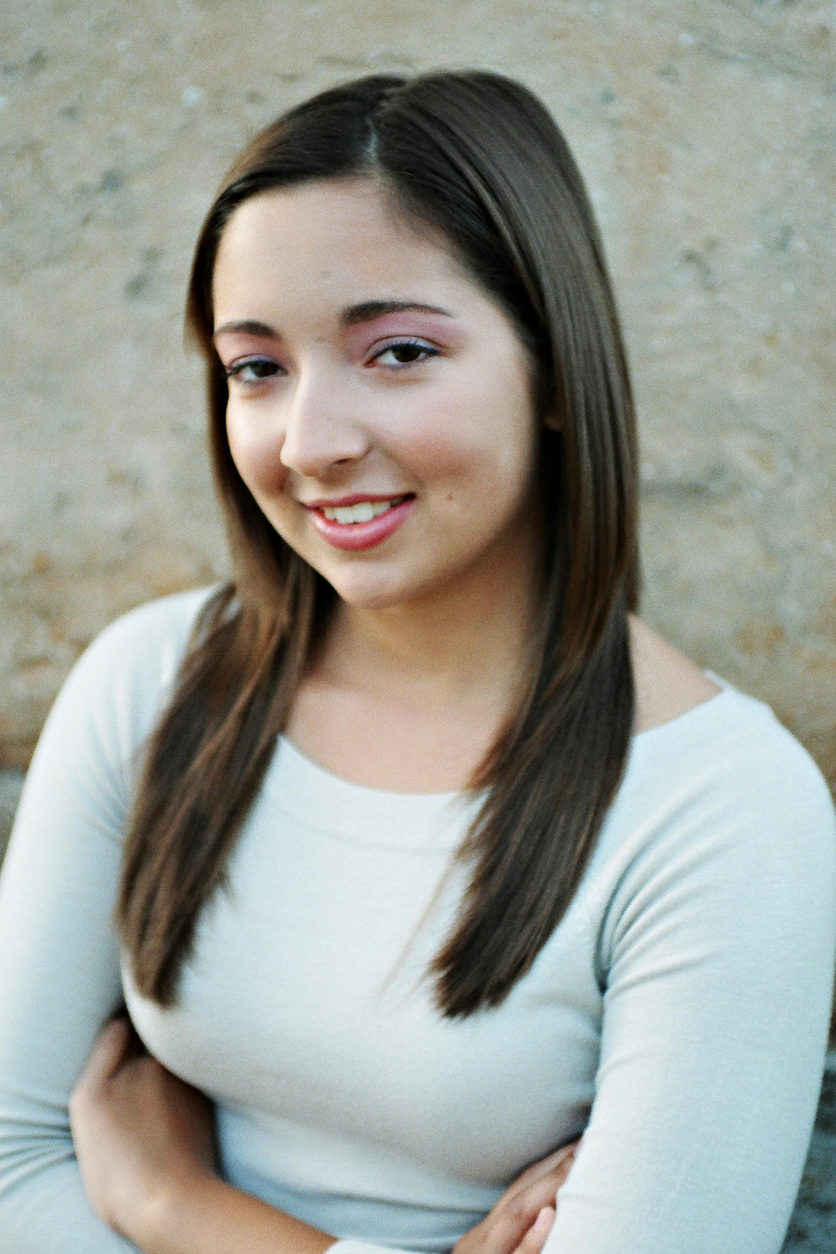 Ilmainen Valkoiseen paitaan pukeutunut nuori nainen hymyilee itsevarmasti neutraalia taustaa vasten. Kuvapankkikuva