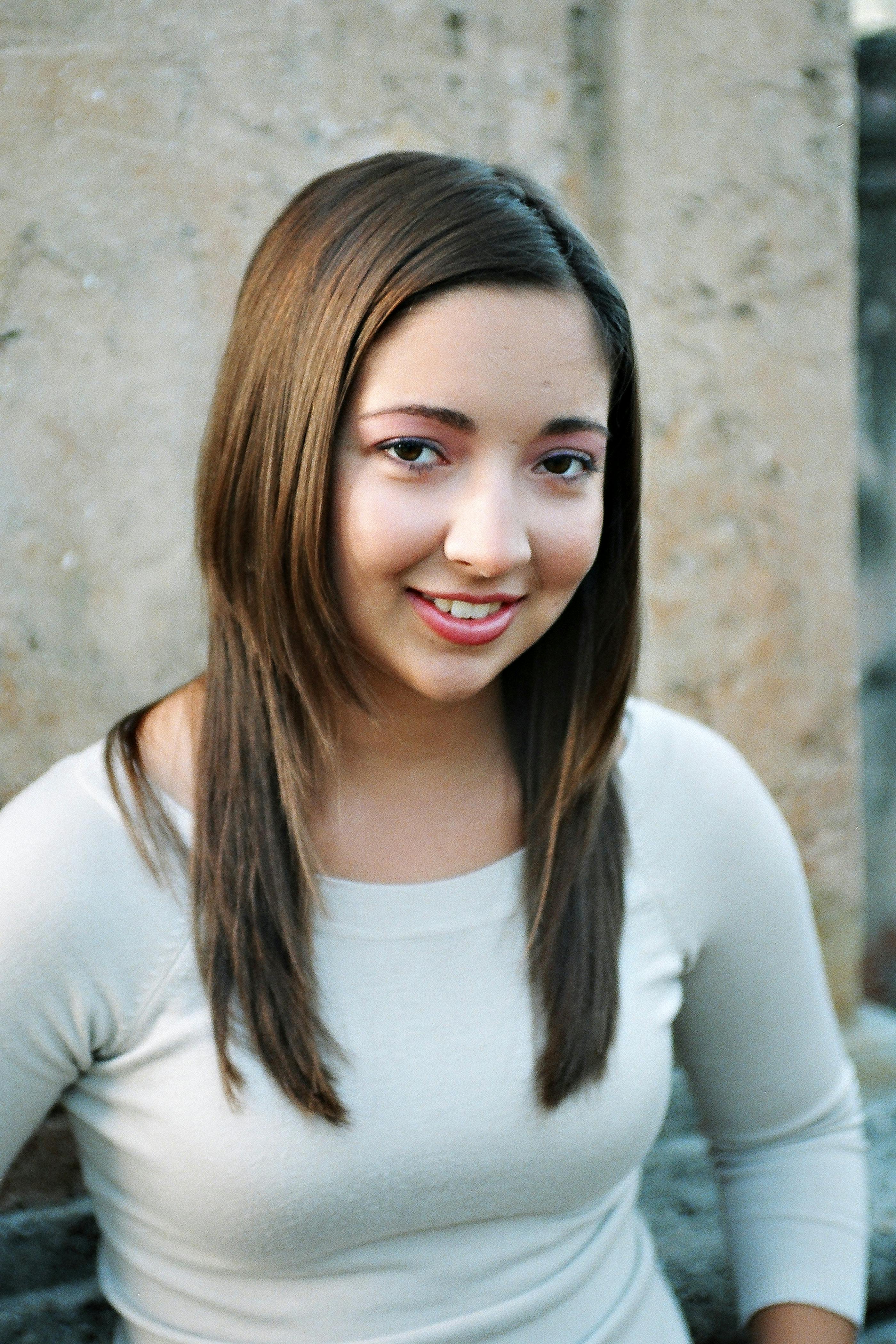 бесплатная Непринужденный портрет улыбающейся молодой женщины с длинными каштановыми волосами на фоне каменной стены. Стоковое фото