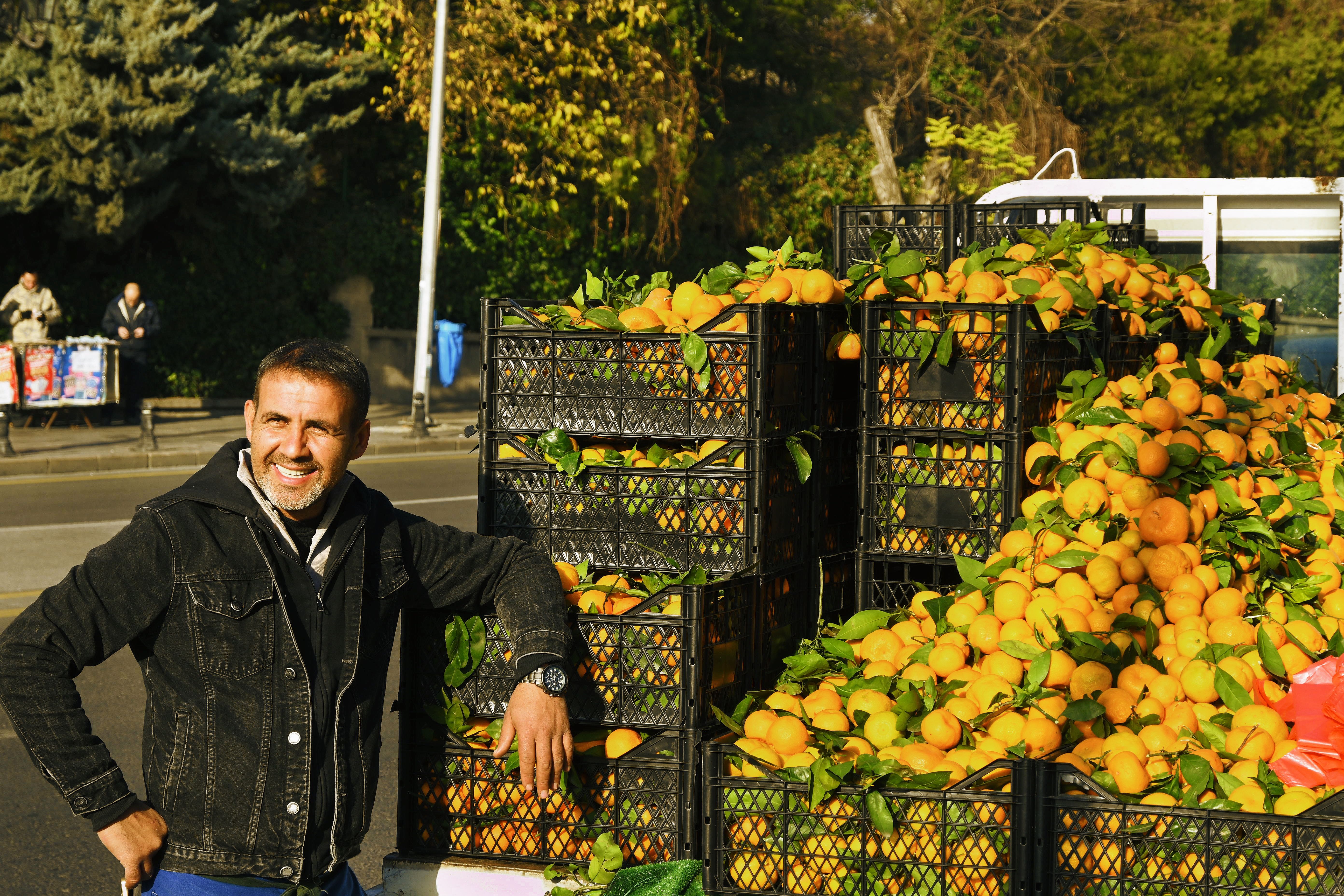 Man smiling by fresh oranges at an outdoor market, showcasing vibrant produce and local trade.