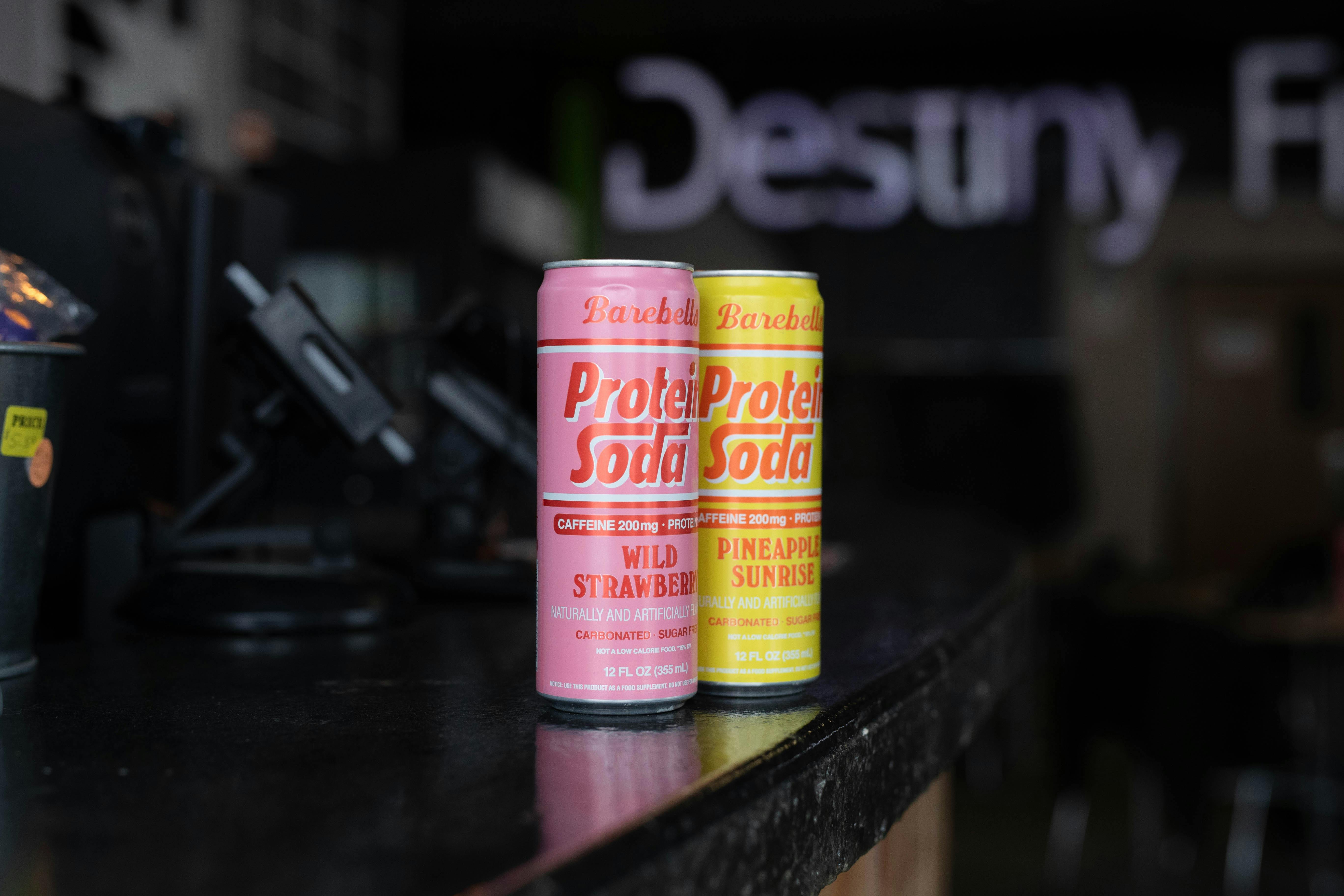 Two Barebells protein soda cans, Wild Strawberry and Pineapple Sunrise, showcased on a counter.
