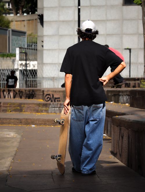 Free A young man holding a skateboard stands in an urban park, exuding a casual street vibe. Stock Photo