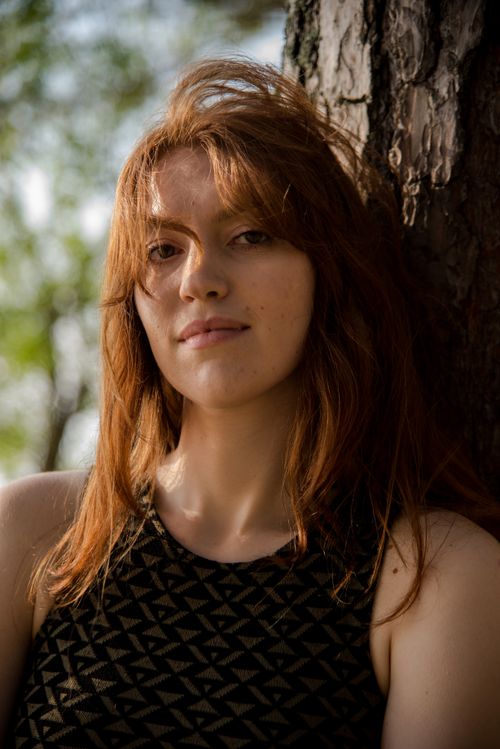 Free Natural light portrait of a woman with red hair leaning against a tree in Estonia. Stock Photo