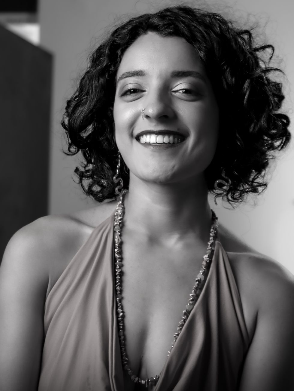 Captivating black and white portrait of a smiling woman with curly hair, exuding elegance.
