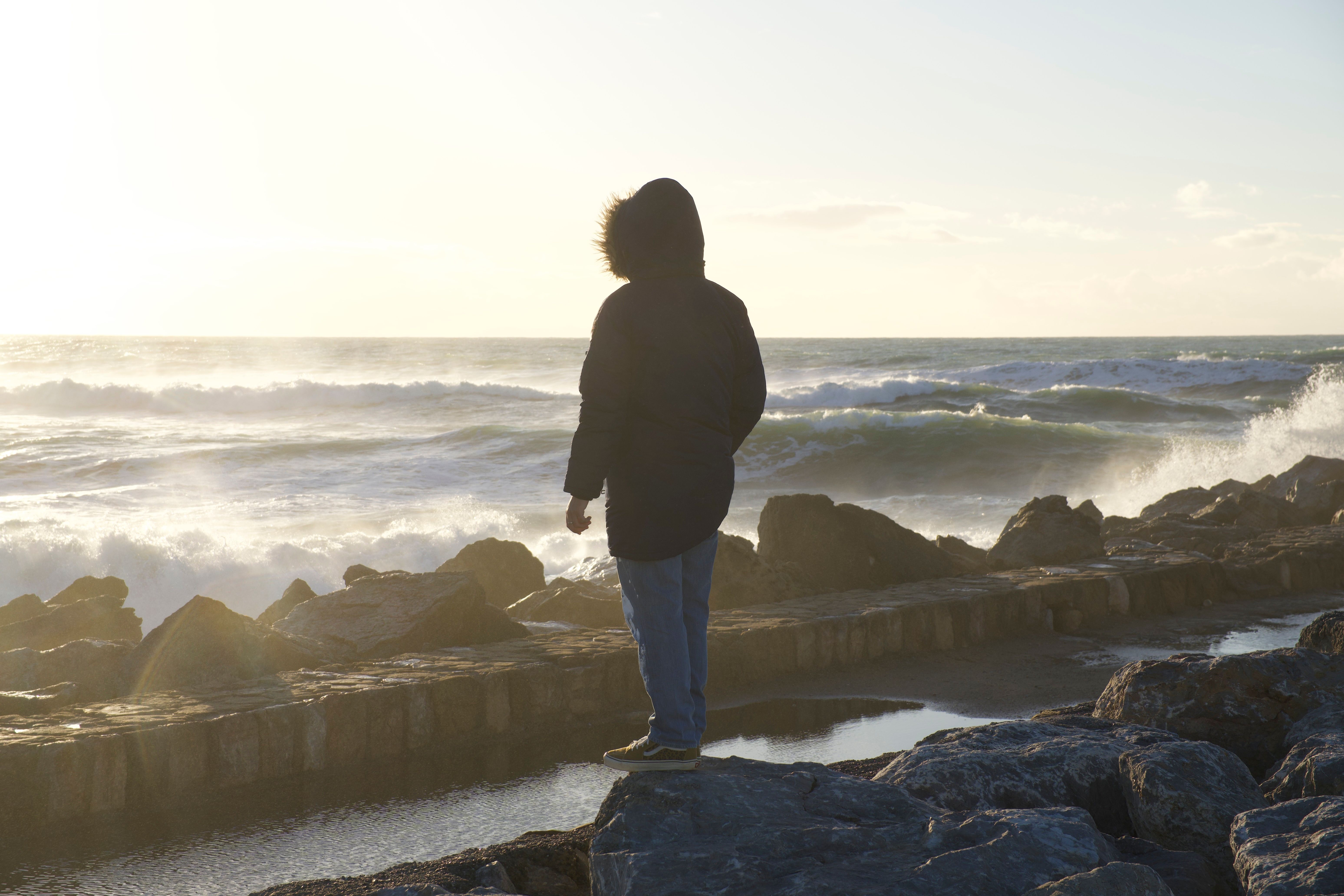 person sitting alone on a rock by a stormy ocean, looking contemplative