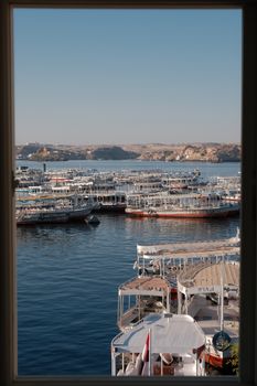 Tranquil scene of multiple boats docked on a lake framed by a window view under a clear sky.