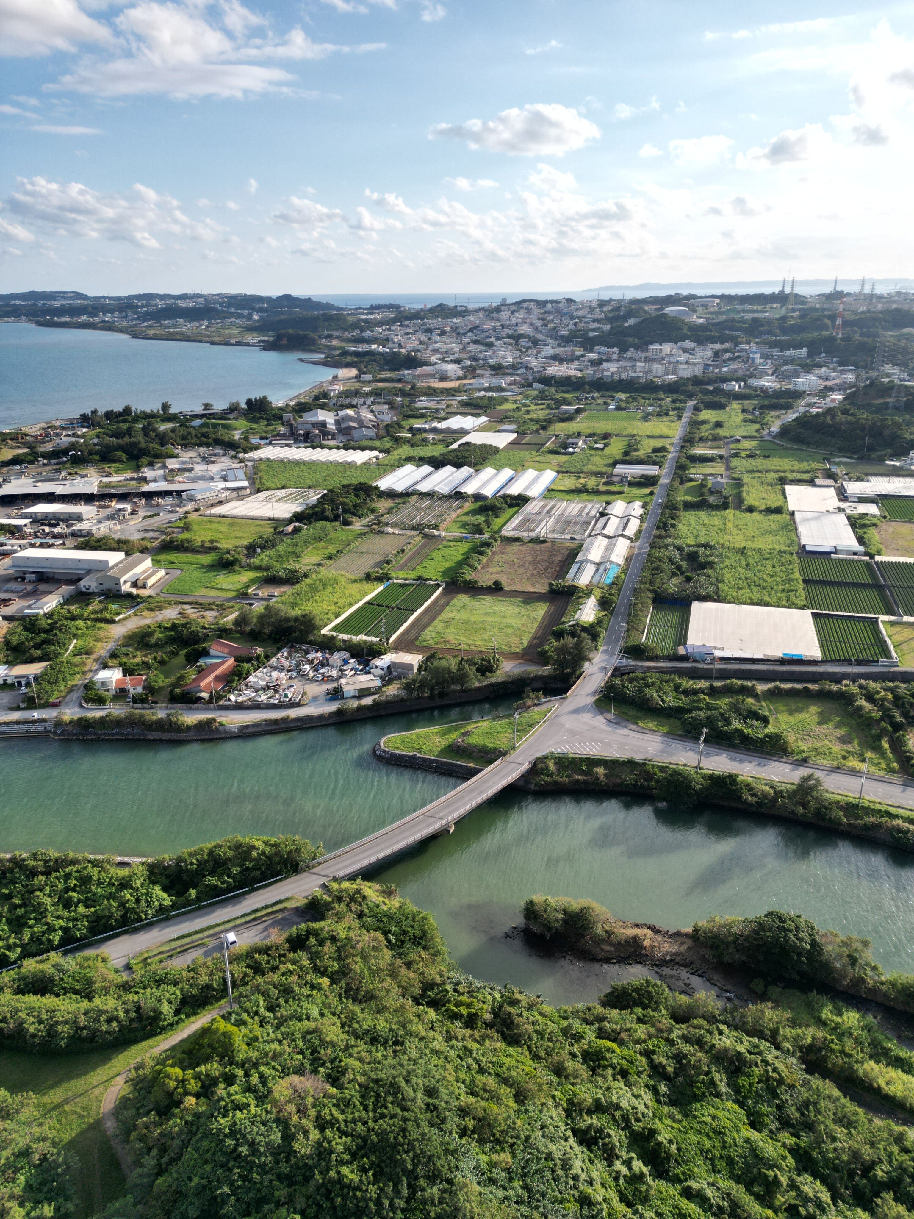 Expansive aerial view of green farmland, a river, and distant cityscape on a sunny day.
