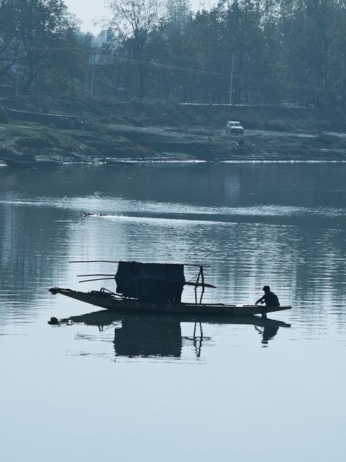 Free Silhouette of a lone fisherman on a boat gliding across a tranquil river under soft daylight. Stock Photo