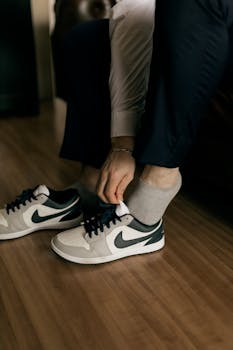 Close-up of a man tying sneakers, focusing on shoes and hands indoors on a wooden floor.