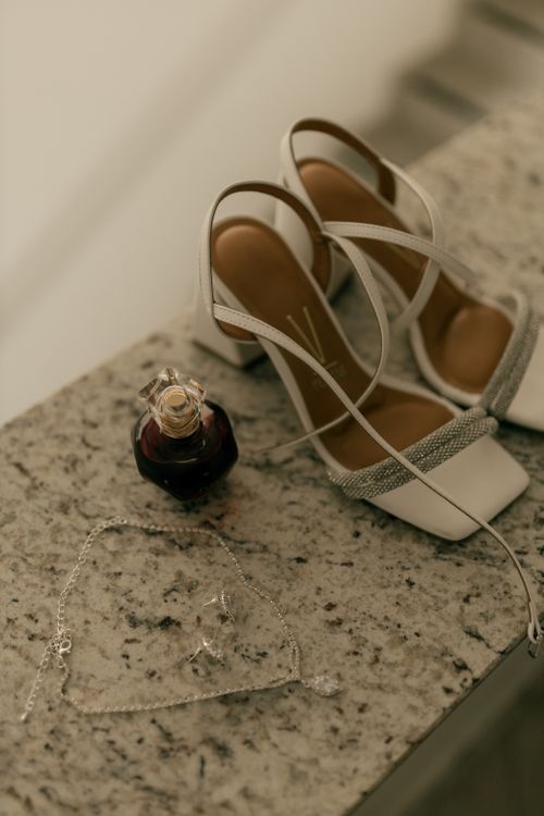 Free Stylish bridal heels, jewelry, and perfume arranged elegantly on a granite surface. Stock Photo