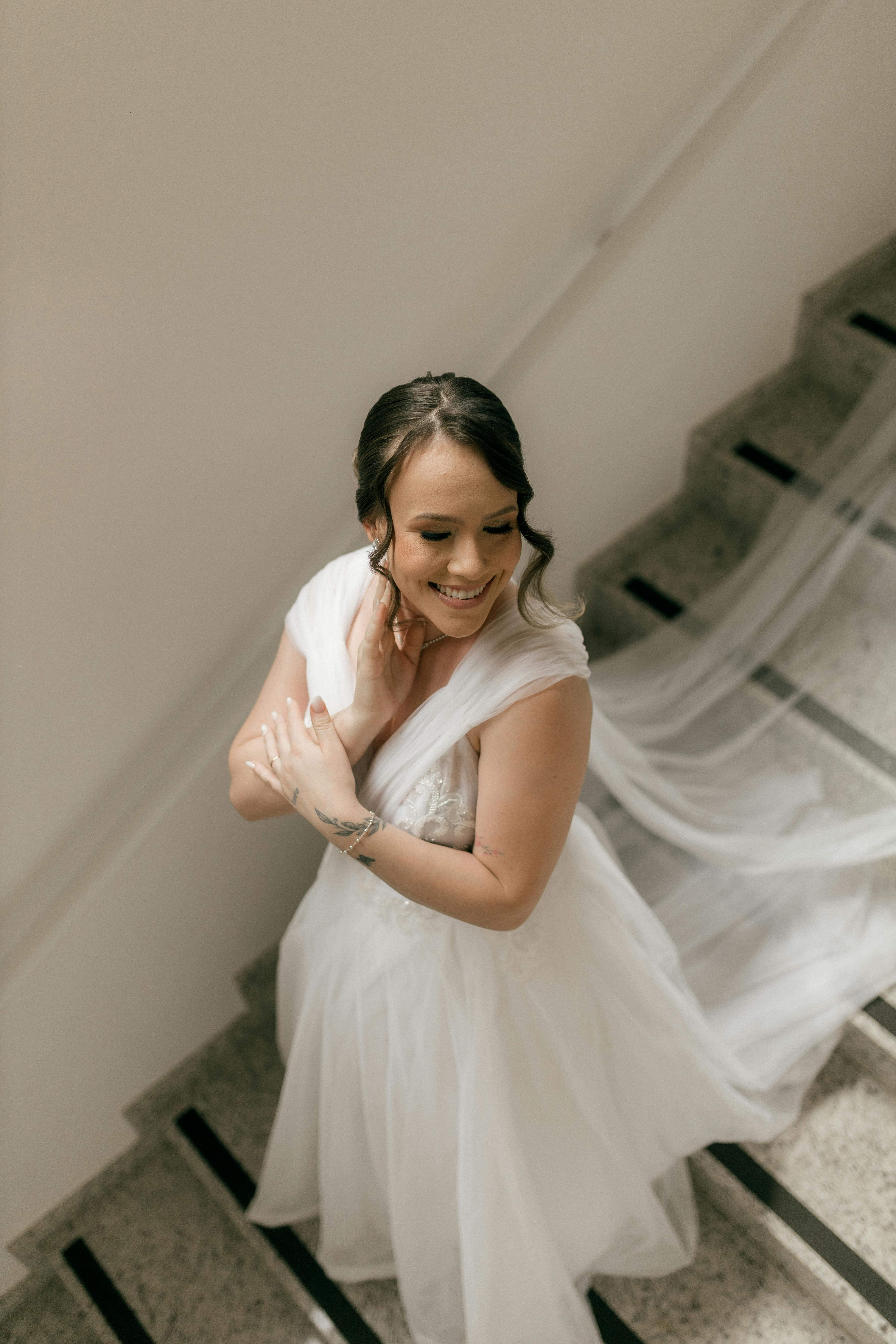 Gratuit Une mariée souriante, vêtue d'une robe blanche fluide, descend un escalier, rayonnante d'élégance et de joie. Photos