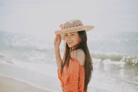阳光明媚的海边，一位戴着帽子的年轻女子微笑着，拥抱夏日的氛围