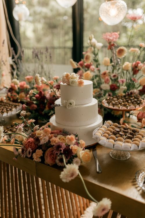 Free Beautiful wedding cake with elegant floral decor surrounded by assorted desserts on a festive table. Stock Photo