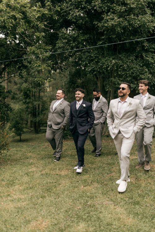 Free Group of groomsmen walking outdoors, dressed in stylish suits, with greenery backdrop. Stock Photo