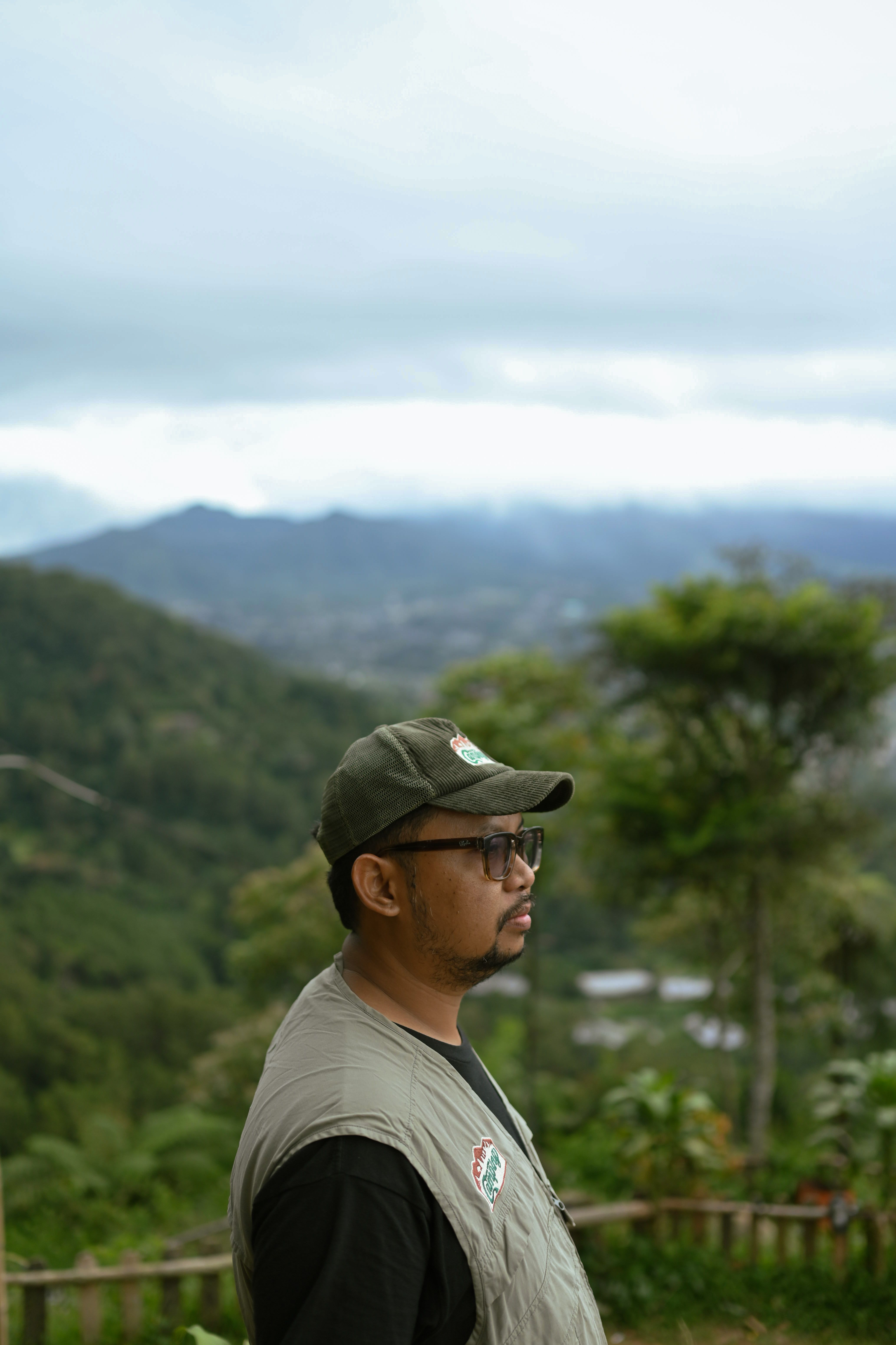 A man stands in a mountain landscape in Indonesia, surrounded by lush greenery and distant hills.