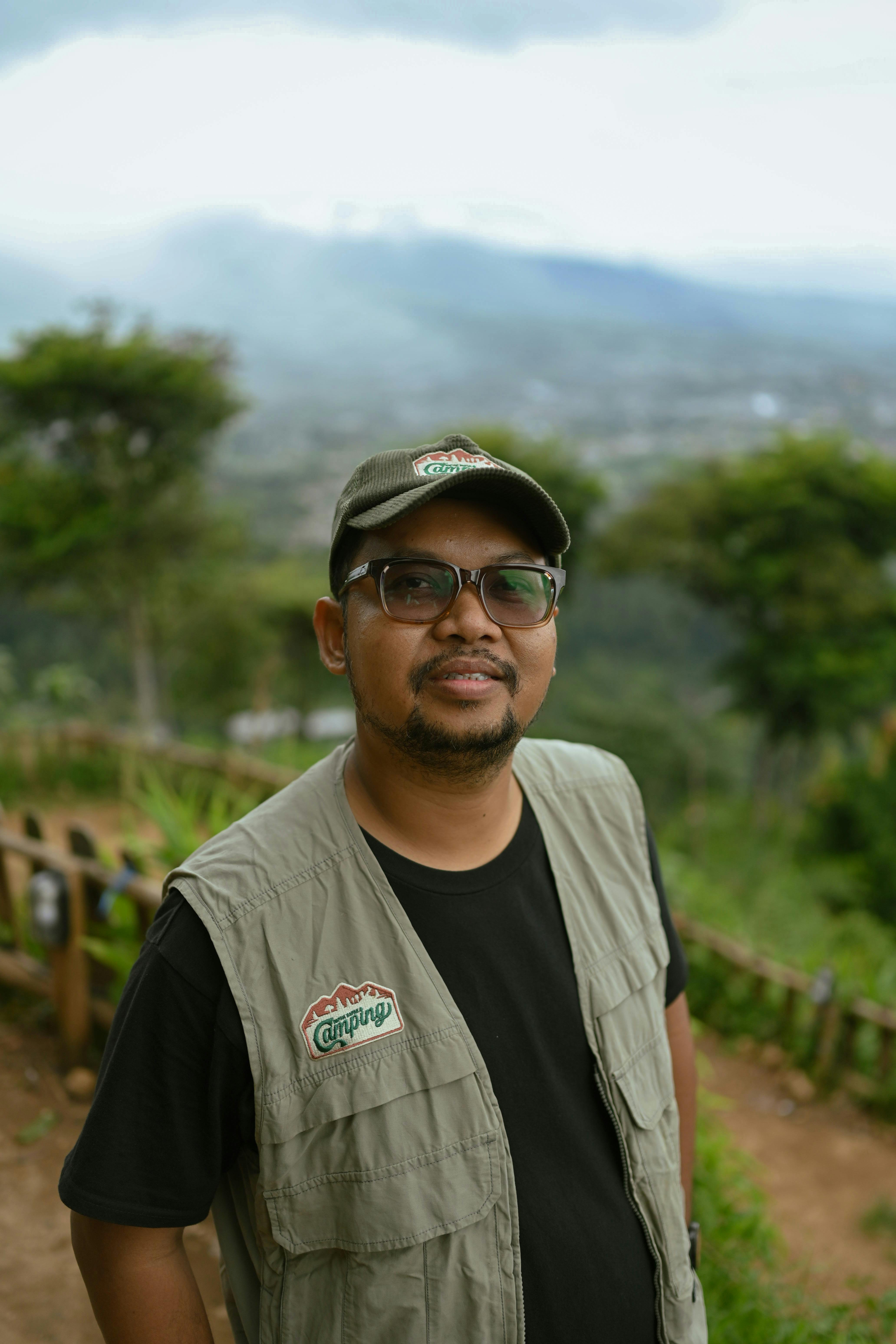 Man standing outdoors with a lush Indonesian landscape backdrop, showcasing nature and casual style.