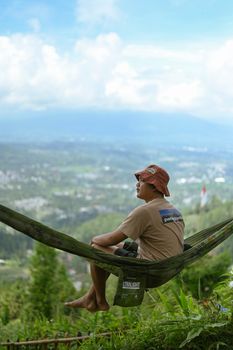 Man enjoying a peaceful moment in a hammock overlooking lush Indonesian scenery. Perfect escape into nature.
