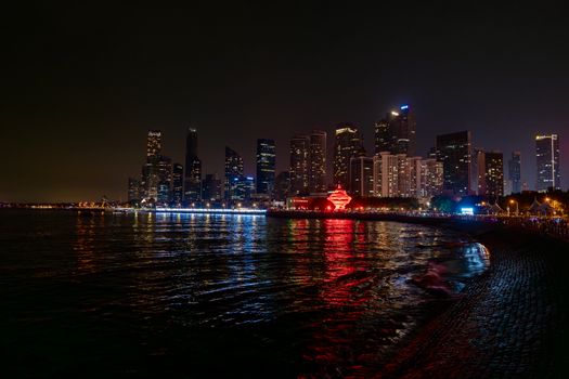 Nighttime cityscape with illuminated skyscrapers reflecting on water, showcasing urban vibrance.