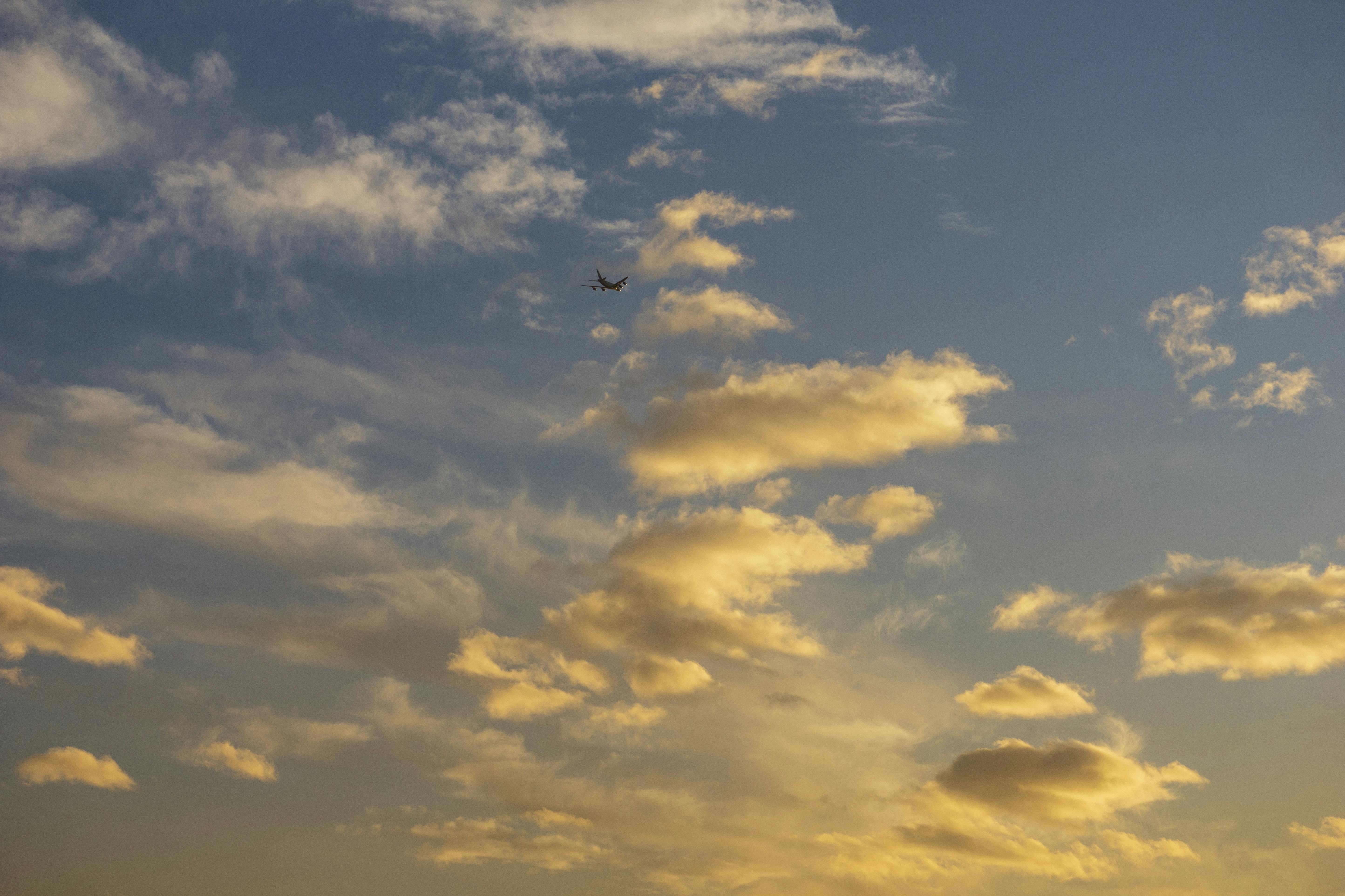 Δωρεάν Ένα αεροπλάνο πετάει ψηλά σε έναν χρυσό ουρανό ηλιοβασιλέματος με ανάγλυφα σύννεφα, δημιουργώντας μια γαλήνια και γραφική θέα. Φωτογραφία από στοκ φωτογραφιών