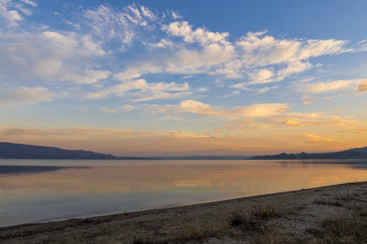 Tranquil sunrise over a calm lake with a sandy beach foreground.