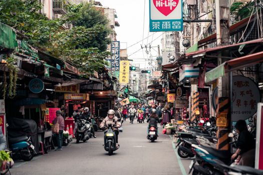 Bustling street market in Taipei, Taiwan, with people and scooters under neon signs.